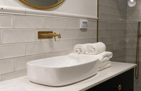 A luxury bathroom lifestyle shot featuring neatly stacked Egyptian cotton towels resting beside a polished stone countertop and brushed brass bathroom fittings.