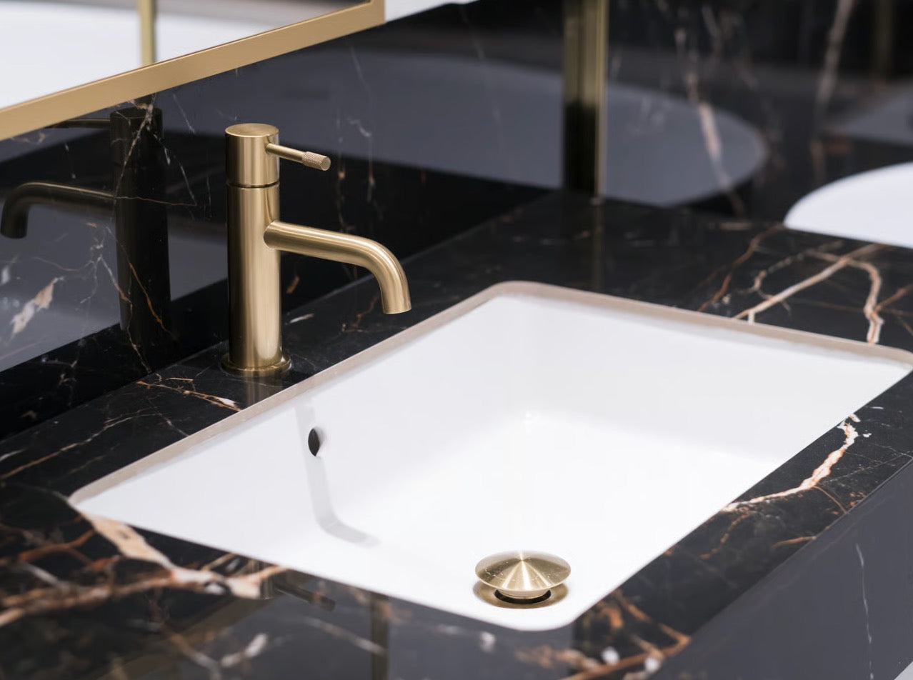 A high-end luxury hotel bathroom detail showcasing premium brushed brass tap hardware set elegantly against a polished black and golden marble vanity.