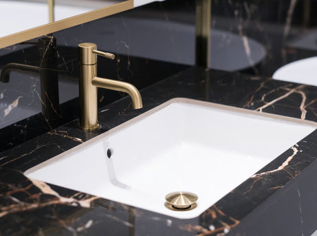 A high-end luxury hotel bathroom detail showcasing premium brushed brass tap hardware set elegantly against a polished black and golden marble vanity.