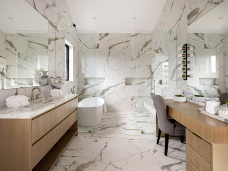 An elegant close-up lifestyle photograph of rich brushed brass bathroom hardware tap fixtures set against a premium Carrara marble surface.