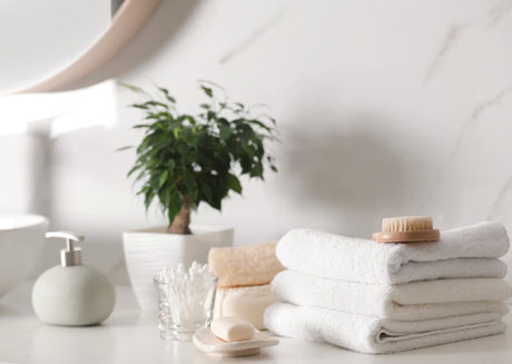 A tranquil luxury spa bathroom setting featuring crisp, fluffy white Egyptian cotton towels stacked neatly on a warm natural stone countertop.