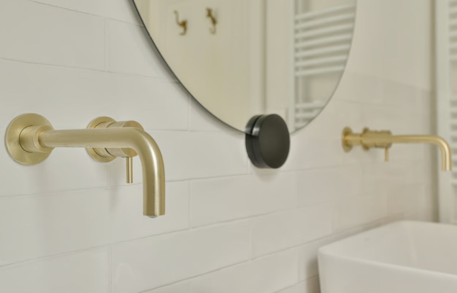 A detailed close-up shot of luxurious brushed brass bathroom taps set against a sleek polished wall tile background.