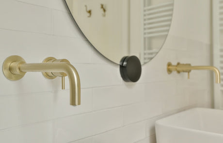 A detailed close-up shot of luxurious brushed brass bathroom taps set against a sleek polished wall tile background.